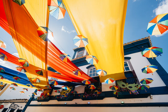 Decora&ccedil;&atilde;o de Carnaval com tecidos vibrantes e sombrinhas de frevo em rua do centro hist&oacute;rico de Tiradentes, com m&aacute;scaras nas sacadas de casar&atilde;o colonial, Minas Gerais, Brasil.