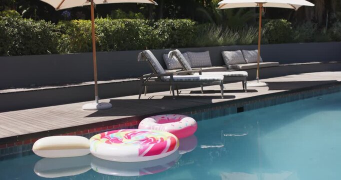 Camera is panning upward to show pool floats, lounge area, parasols, and rising trees