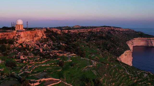 Aerial drone view of the Highest point of Malta at Dingli Cliffs, beautiful lush green grass and rock formations with a steep drop to the sea at sunset, golden hour. Sun giving the golden glow