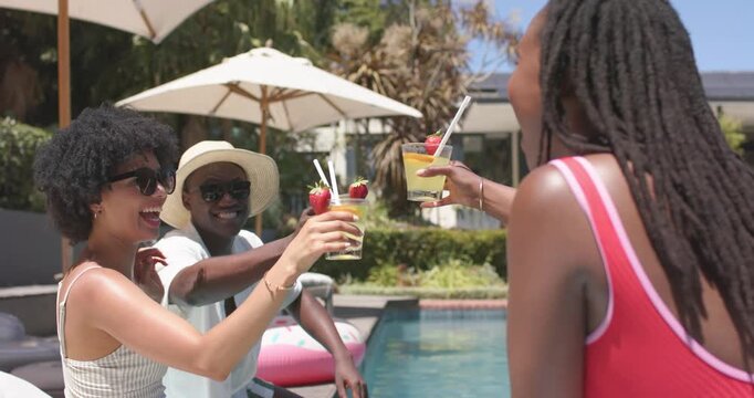 African American friends toasting drinks after right woman in red swimsuit leading cheers poolside