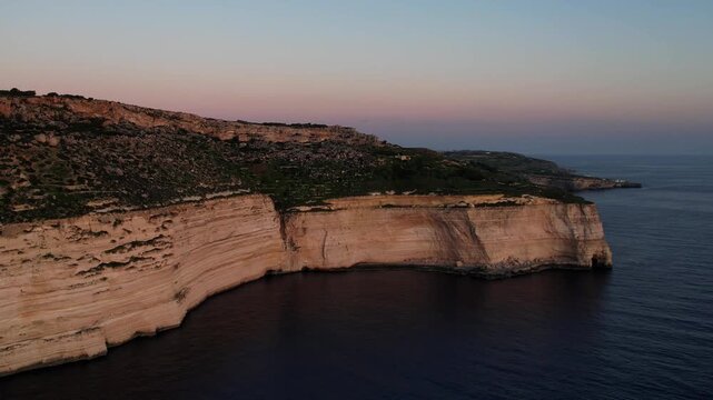 Aerial drone view of the Highest point of Malta at Dingli Cliffs, beautiful lush green grass and rock formations with a steep drop to the sea at sunset, golden hour. Sun giving the golden glow