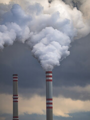Tall industrial chimneys with red and white stripes emitting thick smoke into dark dramatic sky
