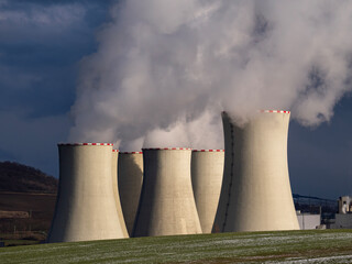 Group of massive cooling towers emitting thick white steam against dark dramatic storm sky