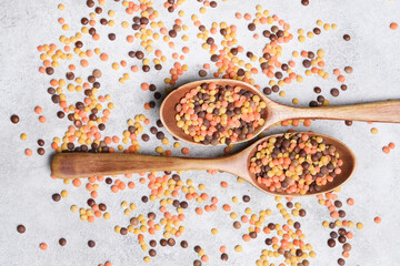 Wooden spoons filled with colorful lentils on a textured surface, scattered lentils around the spoons create a vibrant and visually appealing composition