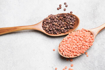 Wooden spoons filled with brown and red lentils on a gray stone surface, scattered lentils around, showcasing the texture and color contrast of the legumes