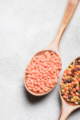Wooden spoon filled with pink lentils and another spoon containing mixed lentils on a light gray surface, showcasing the texture and color variations of legumes