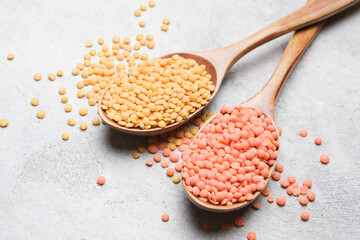 Wooden spoons filled with yellow and pink lentils on a textured gray surface, scattered lentils around the spoons create a vibrant and colorful display of legumes