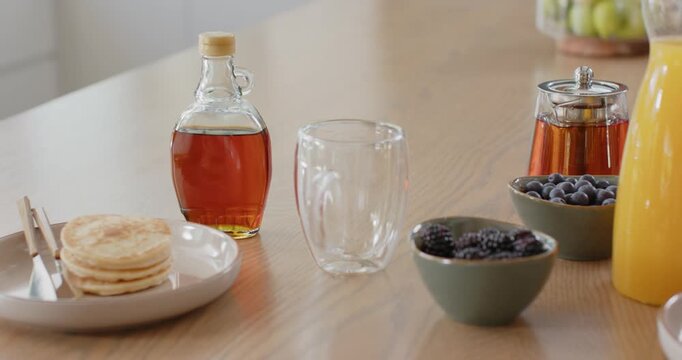 Camera is sliding right, revealing wood counter pancakes, empty glass while showing berries, syrup
