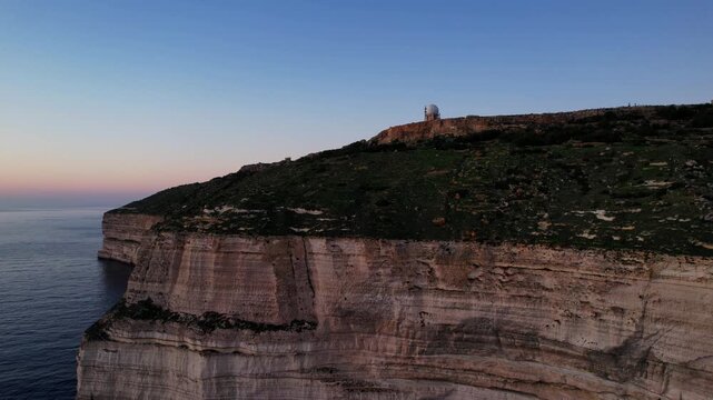 Aerial drone view of the Highest point of Malta at Dingli Cliffs, beautiful lush green grass and rock formations with a steep drop to the sea at sunset, golden hour. Sun giving the golden glow