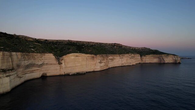 Aerial drone view of the Highest point of Malta at Dingli Cliffs, beautiful lush green grass and rock formations with a steep drop to the sea at sunset, golden hour. Sun giving the golden glow