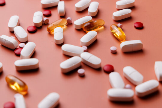 Scattered medical pills of various sizes and colors on a cream gradient background for clinical treatment and health supplement ads.