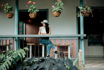 Woman sitting on colonial balcony surrounded by hanging plants. Peaceful travel lifestyle moment in colorful Latin setting. © LuisPimenttel