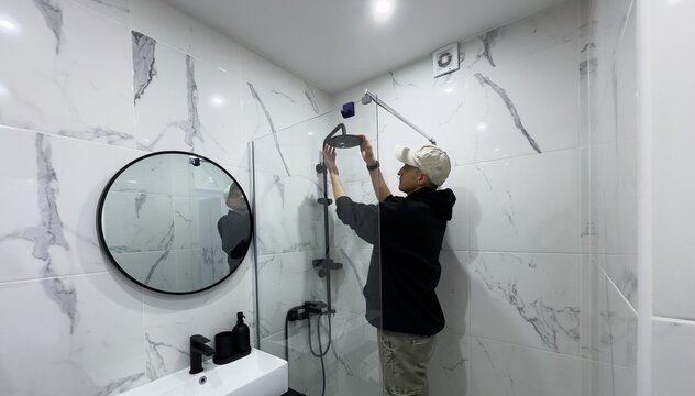 Professional handyman working in shower booth indoors, space for text