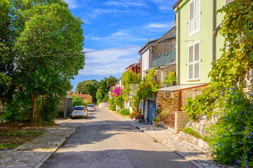Fototapeta premium A picturesque residential street with colorful flowers and stone walls in the coastal town of Piran, Slovenia, on the Istrian peninsula. 