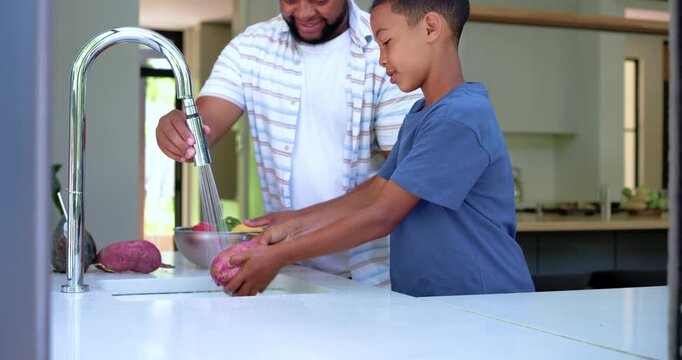 African American father-son washing purple tubers at island sink with bowl, faucet running for meal