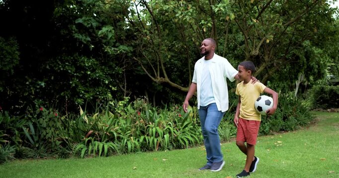African American father  and  son walking yard dad pointing guiding son kicking soccer ball, copy sp