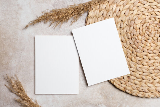 Wedding invitation or graating or flyer card mockup with two blank cards on a woven placemat with dried grass decor, ideal for customizable designs and elegant stationery presentations
