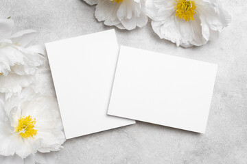 Obraz premium Blank wedding invitation cards mockup with white peony flowers, two cards front and back sides with copy space for design presentation