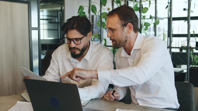 Two men review documents and discuss tasks in a modern office space during a work meeting in the morning