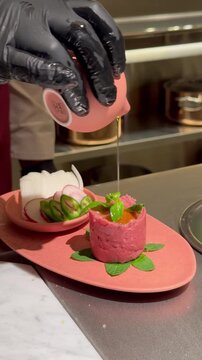 Close-up of chef garnishing a Lebanese Kibbeh Nayyeh dish with olive oil, fine dining presentation.