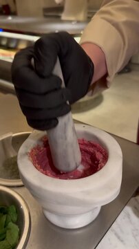 Chef using a traditional marble mortar and pestle to grind Kibbeh Nayyeh, authentic Middle Eastern food preparation.