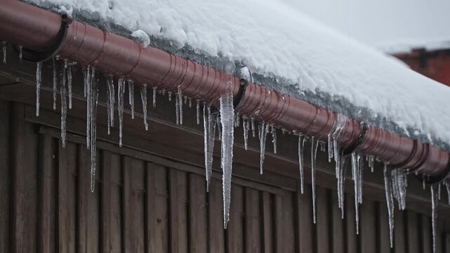 Long Hazardous Icicles Hanging from Frozen Rain Gutter Over Street Sidewalk Posing Injury Danger for Pedestrians