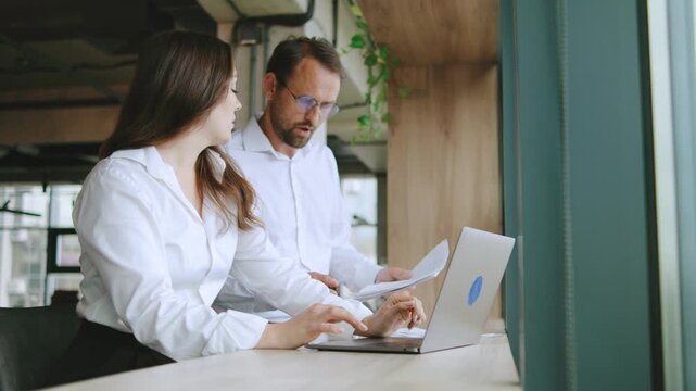 Business team discusses work tasks while sitting at a table near a large window in a modern office during the day