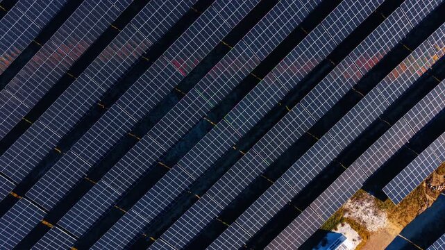 Aerial view of geometric solar panel rows. Symmetrical pattern of dark photovoltaic panels arranged in parallel rows with ground between them.