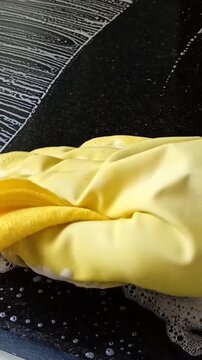 Scrubbing a black granite countertop with soap and yellow gloves.