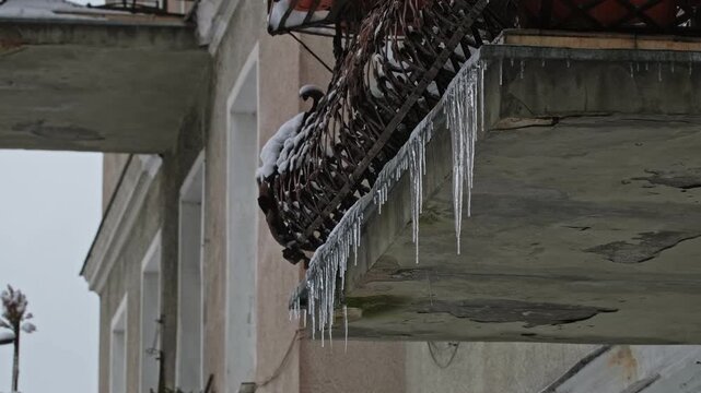 Long Hazardous Icicles Hanging from Frozen Balcony Edge Over Street Sidewalk Posing Injury Danger for Pedestrians
