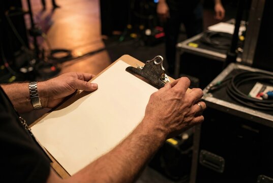 Stage manager or event crew member holding a clipboard with a blank sheet of paper backstage.