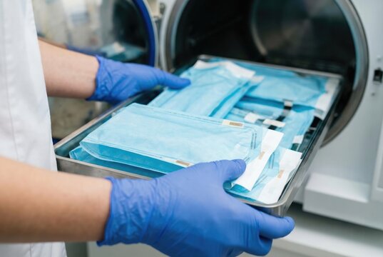 Medical worker in blue gloves loading sealed sterile instrument pouches into an autoclave for sterilization.