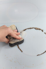Woman cleaning electronic ceramic stove surface using sponge