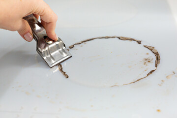 Woman cleaning electronic ceramic stove surface using special steel scraper