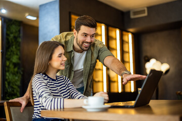 Young man showing something on a laptop screen to his girlfriend in a cafe.