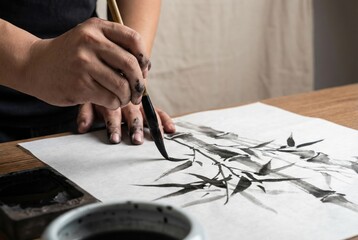 Obraz premium Artist's hands painting traditional Japanese or Chinese bamboo sumi-e ink wash painting.
