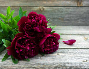 Deep red peonies with green leaves arranged on a rustic wooden background