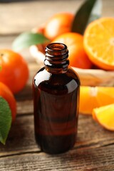 Bottle of tangerine essential oil and fresh fruits on wooden table, closeup