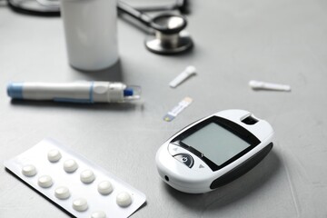 Diabetes. Digital glucometer, pen, test strip, lancets and pills on gray textured table, closeup