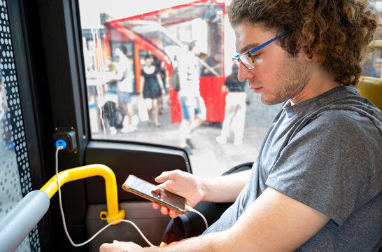 Berlin, germany, august 14, 2023. Young man riding a bus and charging his mobile phone using an onboard usb port, focusing on connectivity during travel