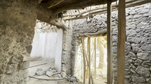 Camera tracks backward revealing the interior of the House of Kulthum ibn al-Hadm in Quba, showing ancient stone masonry, mud walls, and traditional wooden roof beams significant to Islamic heritage.
