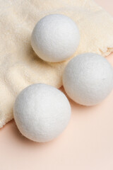 White wool laundry dryer balls placed on a soft beige towel against a light pink background, showcasing their round shape and texture for laundry care