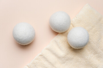Wool laundry dryer balls arranged on a soft beige towel against a light pink background, showcasing their round shape and texture for laundry care