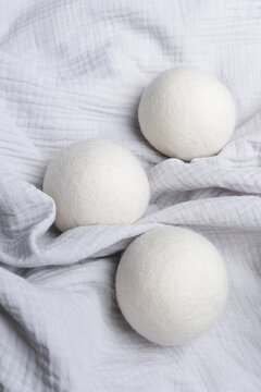 Wool laundry dryer balls arranged on a soft, textured white fabric, showcasing their round shape and natural fibers in a clean, minimalist setting