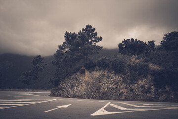 Mountain road curve with trees and rocky hillside under cloudy sky