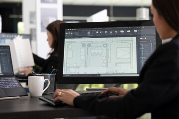 Young female architect reviews digital floor plans on monitor before construction deadline....