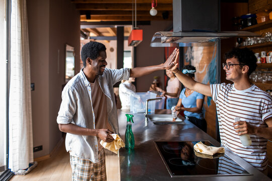 Roommates high-five while cleaning modern kitchen
