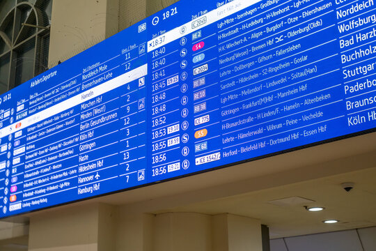 Digital departure board Hannover Hauptbahnhof, displaying train schedules with destinations, DB logo, blue screen interface, Multilingual real-time transit information commuters in Germany, Hannover