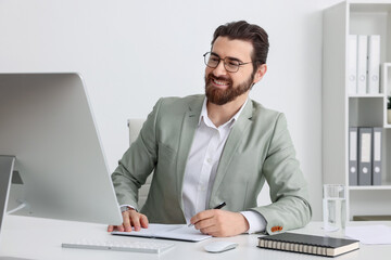 Fototapeta premium Businessman working with computer and writing at table near white wall indoors