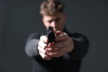 Dangerous criminal holding gun on grey background, selective focus. Armed robbery